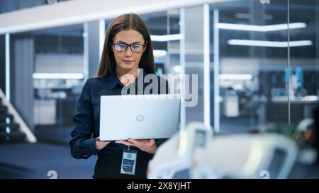 Portrait d'une belle femme caucasienne portant des vêtements d'entreprise intelligents et des lunettes, à l'aide d'un ordinateur portable. Femme d'affaires, responsable des technologies de l'information, spécialiste en ingénierie robotique. Banque D'Images