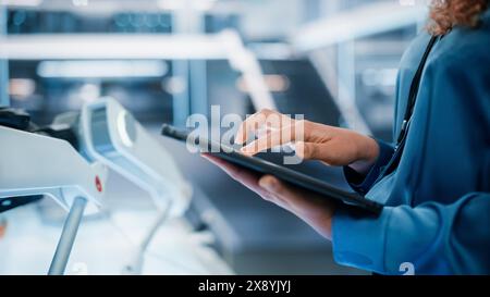 Gros plan d'une femme tenant et utilisant un ordinateur tablette dans un bureau industriel moderne de haute technologie. Mains d'une femme naviguant sur Internet, balayant dans la base de données de messagerie d'entreprise. Banque D'Images