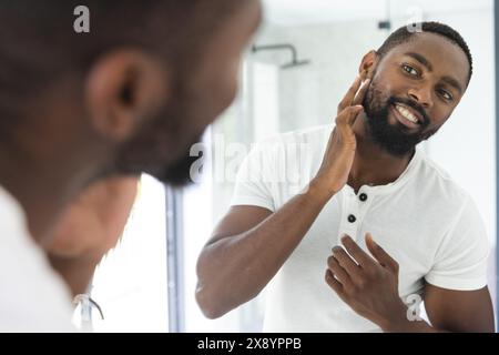 L'homme afro-américain vérifie son visage dans le miroir à la maison Banque D'Images