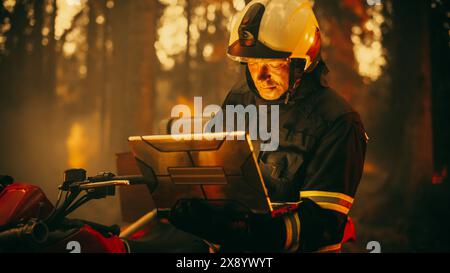 Portrait d'un pompier dans un équipement de sécurité à l'aide d'un ordinateur portable robuste, rapport sur une situation avec un incendie dangereux de Wildland dans une forêt. Dure journée au travail pour un pompier volontaire courageux. Banque D'Images