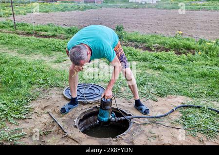 Travailleur pompant les déchets d'eaux usées de la fosse septique avec la pompe d'eaux usées à travers le trou de maintenance. Banque D'Images