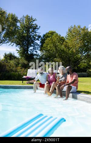 En plein air, divers amis seniors riant au bord de la piscine, partageant des blagues Banque D'Images