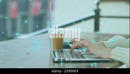 Image d'un réseau d'icônes numériques tournant sur la section médiane d'une femme à l'aide d'un ordinateur portable dans un café Banque D'Images