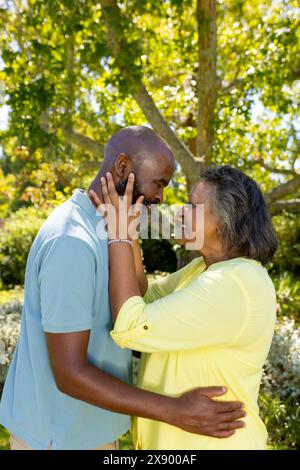 Couple senior diversifié embrassant à l'extérieur dans un jardin ensoleillé Banque D'Images