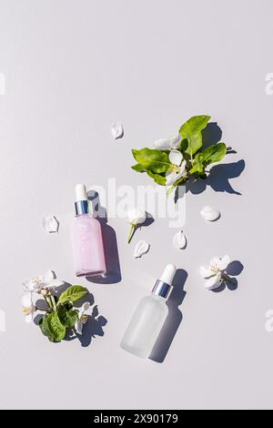 Deux bouteilles chics avec un produit cosmétique pour le soin des jeunes peaux sur un fond clair avec des brins de pommiers en fleurs. vue de dessus verticale Banque D'Images