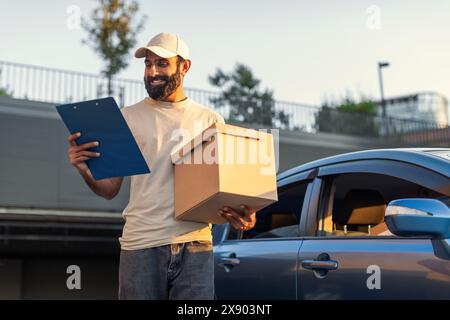 Livreur tenant paquet et presse-papiers à côté de la voiture Banque D'Images