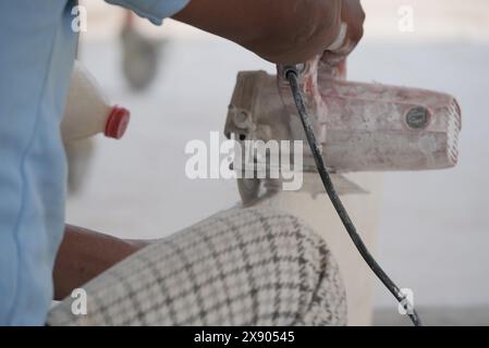 Un gros plan détaillé capture un artisan qualifié utilisant une scie électrique portative pour couper précisément une tuile, avec de la poussière et des débris dispersés autour. La mise au point Banque D'Images