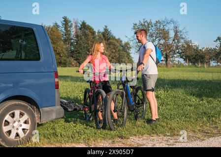 Jeune homme et une femme qui se préparent au vélo tout-terrain, en descendant les vélos de montagne électriques du porte-vélos sur le camping-car. Banque D'Images