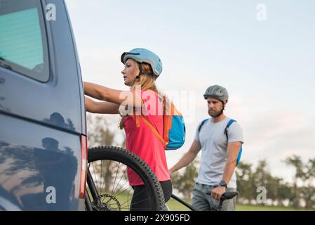 Jeune homme et une femme qui se préparent au vélo tout-terrain, en descendant les vélos de montagne électriques du porte-vélos sur le camping-car. Banque D'Images