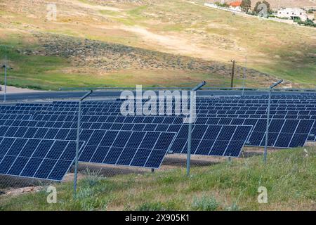 Une vaste gamme de panneaux solaires est située près d'une autoroute, exploitant l'énergie solaire dans un paysage rural, avec des collines ondulantes et des bâtiments clairsemés dans le Banque D'Images