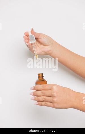 Gros plan des mains d'une femme tenant compte-gouttes et bouteille ambre avec sérum de soin de la peau – concept beauté et bien-être Banque D'Images