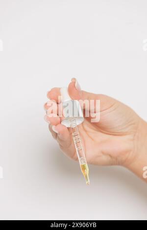 Gros plan de la main d'une femme tenant un compte-gouttes avec sérum de soin de la peau – concept beauté et auto-soin Banque D'Images