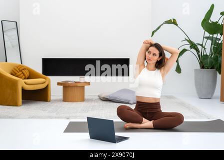 Jeune femme faisant de l'exercice à la maison et regardant des cours en ligne à l'aide d'un ordinateur portable. Copier l'espace. Banque D'Images