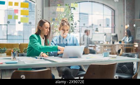 Portrait de deux collègues créatifs collaborant et pointant vers l'ordinateur portable dans Modern Office. Une femme Manager consulte le chef de projet White, ils réfléchissent sur le projet. Banque D'Images
