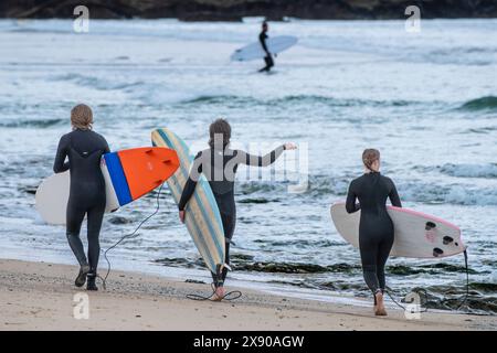 Trois surfeurs portant leurs planches de surf marchant le long du rivage sur la plage de Fistral à Newquay en Cornouailles au Royaume-Uni. Banque D'Images