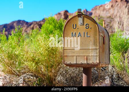 Nelson, Nevada - 15 avril 2024 : la boîte aux lettres US mail en métal rouillé se trouve sur un seul poste au milieu d'arbustes verts avec un terrain rocheux et un SK bleu clair Banque D'Images