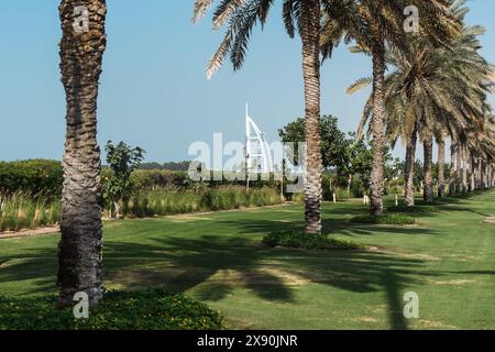 Dubaï, Émirats arabes Unis - 6 janvier 2024 : L'emblématique Burj Al Arab se dresse au-delà du sentier luxuriant bordé de palmiers sous un ciel bleu clair. Banque D'Images