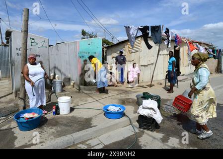 Scène de rue typique dans une zone non développée à Khayelitsha. Plusieurs ménages d'habitation en cabane partagent les robinets d'eau communaux, les toilettes, etc Banque D'Images