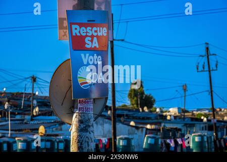 Khayelitsha. Affiches électorales pour divers partis se bousculant pour l'espace sur les pôles et les votes des peuples lors des élections de mai 29/2024 en Afrique du Sud. En arrière-plan les cabanes et les toilettes extérieures du canton. Banque D'Images