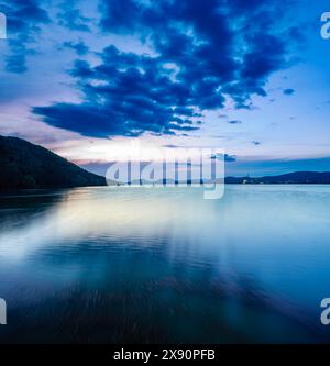 Une scène nocturne tranquille sur Embalse de Puente Nuevo reflétant un ciel bleu éclatant et des montagnes silhouettes. Banque D'Images