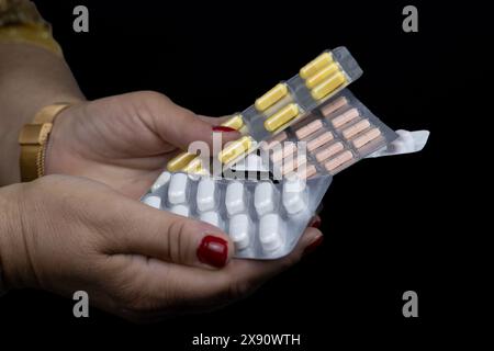 Cette image capture une vue rapprochée des mains d’une femme tenant plusieurs blisters de différentes pilules Banque D'Images