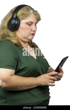 Cette photographie capture une femme blanche caucasienne d’âge moyen immergée dans le monde numérique à travers son smartphone tout en portant un casque Bluetooth. Banque D'Images