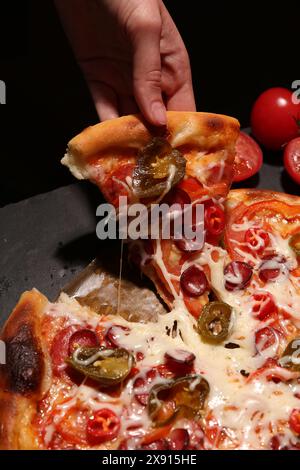 Femme prenant un morceau de délicieuse pizza Diablo sur fond noir, gros plan Banque D'Images