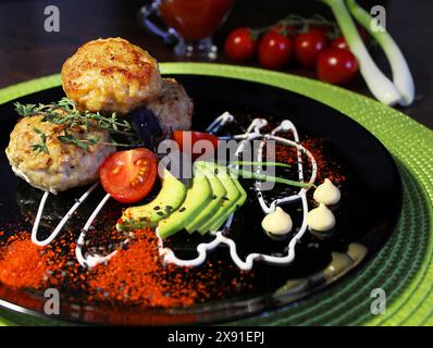 Plat gastronomique composé de galettes de viande, de tranches d'avocat, de tomates et d'échalotes élégamment présentés sur une assiette noire Banque D'Images