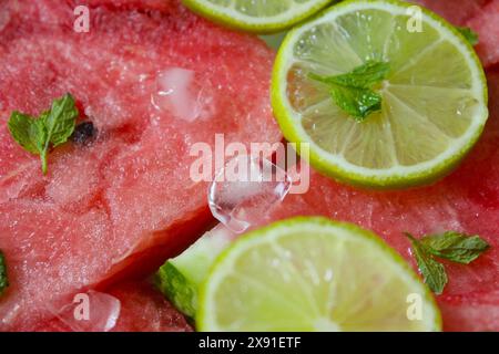 Gros plan de tranches de pastèque avec des tranches de citron vert, des feuilles de menthe et de la glace, créant un look estival rafraîchissant Banque D'Images