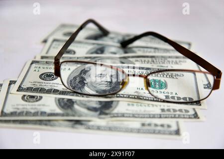 Gros plan de lunettes reposant sur une pile de billets de 100 dollars sur un fond blanc Banque D'Images