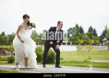 Mariée et mariée en tenue de mariage, debout de manière ludique à l'extérieur sur une journée ensoleillée avec de la verdure en arrière-plan, Biélorussie, Minsk Banque D'Images