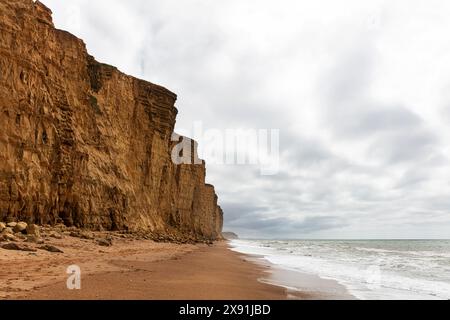 Falaises de West Bay, Dorset, Angleterre les sables dorés s'étendent le long des falaises imposantes sous un ciel partiellement nuageux. Le littoral est rencontré par un doux Banque D'Images