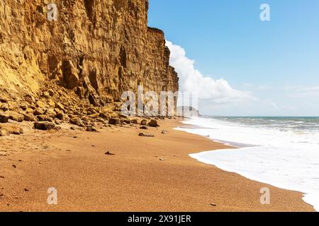 Falaises de West Bay, Dorset, Angleterre les sables dorés s'étendent le long des falaises imposantes sous un ciel partiellement nuageux. Le littoral est rencontré par un doux Banque D'Images