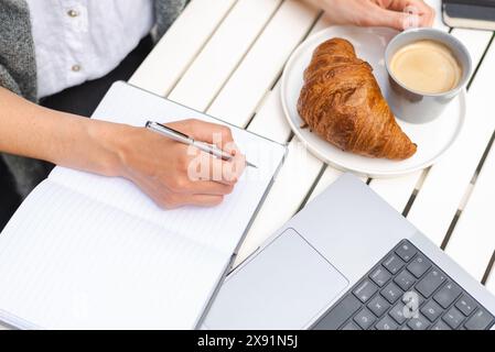 Une femme travaille sur un ordinateur portable, prend des notes et boit du café pendant une réunion dans un café. Banque D'Images