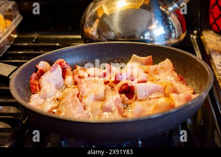 Une livre de frites de bacon coupées épaisses dans une poêle sur une cuisinière à gaz. Banque D'Images