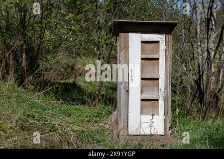 Toilettes en bois dans la forêt. Toilettes avec une porte blanche fermée près des arbres sur l'herbe verte. Banque D'Images