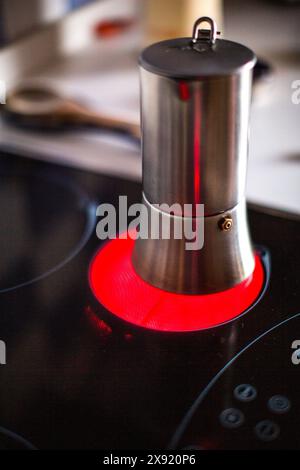 Un pot de moka en acier inoxydable chauffe sur une cuisinière à induction en céramique à éclairage rouge, préparant du café en Espagne. Banque D'Images