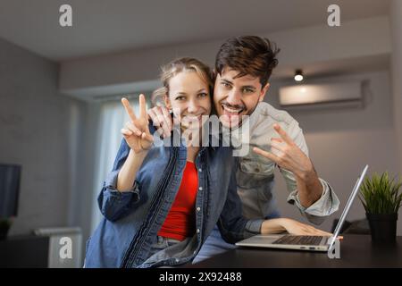 Un jeune couple heureux pose pour un selfie ludique dans leur bureau à domicile, mettant en valeur la joie et l'unité alors qu'ils prennent une pause du travail. Banque D'Images