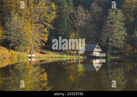 Scène de lac avec forêt d'automne, réflexion dans l'eau et chalet en bois sur la rive du lac. Banque D'Images