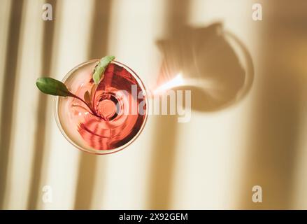 Un verre de jus de betterave provenant de feuilles de betterave fraîches à la lumière directe du soleil projette une ombre sur un fond beige. Banque D'Images