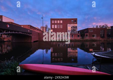 Pays-Bas, Amsterdam - 10 avril 2024 : bâtiments résidentiels et architecture moderne en briques avec vue sur le canal dans le district d'Ijburg au crépuscule Banque D'Images