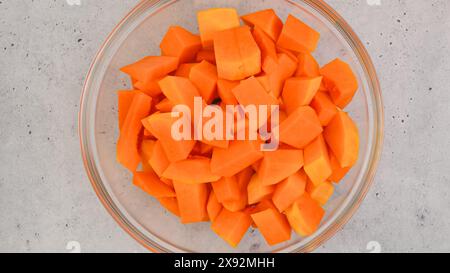 Recette de soupe de courge butternut. Cubes de courge musquée pelés et sans pépins dans un bol en verre gros plan sur la table de la cuisine Banque D'Images