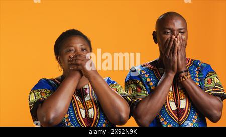 Couple ethnique faisant trois singes sages symbole sur la caméra, montrant le signe de ne pas entendre, voir ou parler en studio. Homme et femme afro-américains couvrant leurs yeux, leur bouche et leurs oreilles. Banque D'Images