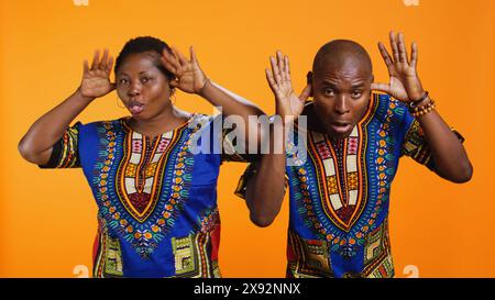 Un couple afro-américain idiot qui se moque devant la caméra, qui sort la langue et s'amuse avec des blagues en studio. Homme ethnique et femme riant ensemble et agissant de manière ludique. Banque D'Images