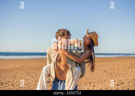 Couple hispanique multiculturel partage un regard aimant tandis que le petit ami porte son partenaire piggyback sur la plage par une journée d'été ensoleillée. Leurs yeux re Banque D'Images