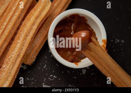 Churro avec dulce de leche sur la pointe et plus de churros sur un fond noir Banque D'Images