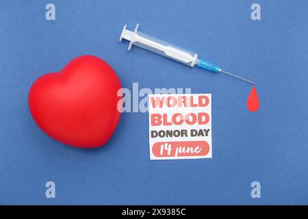 Composition avec goutte de papier, coeur, seringue et feuille de papier avec texte WORLD BLOOD DONOR DAY 14 JUIN sur fond bleu, gros plan Banque D'Images