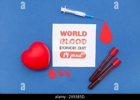 Composition avec des gouttes de papier, coeur, tubes à essai, seringue et feuille de papier avec texte WORLD BLOOD DONOR DAY 14 JUIN sur fond bleu Banque D'Images
