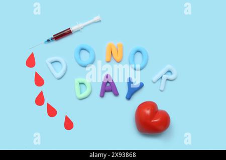 Composition avec coeur, gouttes de papier, seringue et lettres JOUR DONNEUR sur fond bleu Banque D'Images