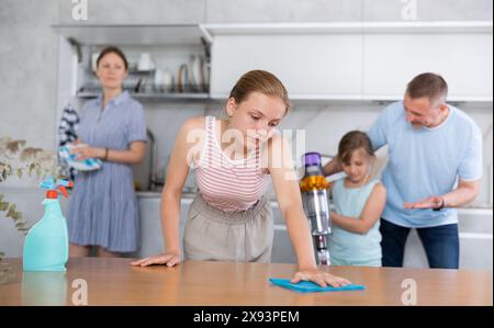 Adolescente nettoie la table avec un chiffon, cuisine propre familiale en arrière-plan Banque D'Images